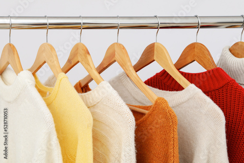 Wardrobe rack with hangers with sweaters on light background