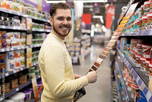 satisfied customer looking at camera at hardware store next to rows of renovation paint