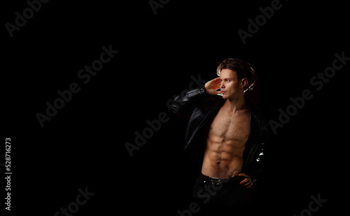handsome macho man with a naked torso in a black leather jacket on a dark background