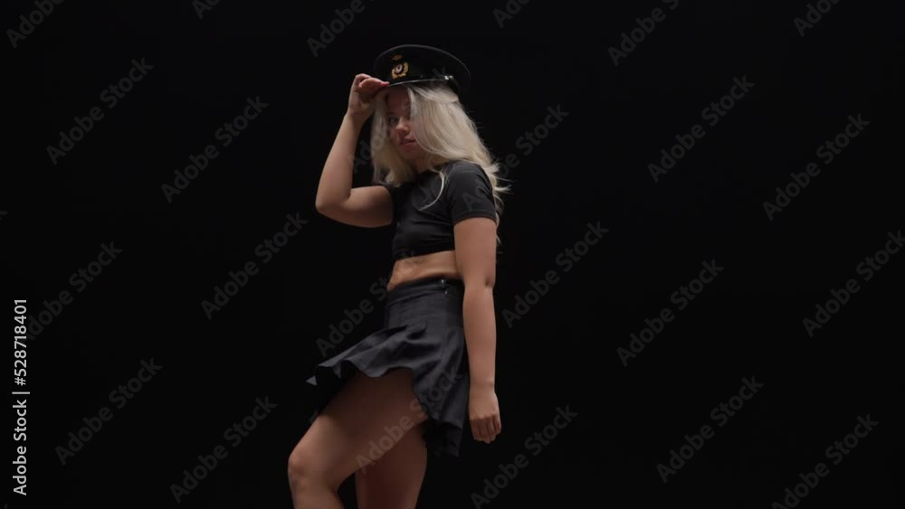 Young Woman in Policemans Hat Dances in Studio Against Black Background Young Woman in Policemans Hat Dances in Studio Against Black Background