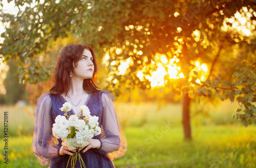 young beautiful woman in blue vintage dress with white flowers at sunset