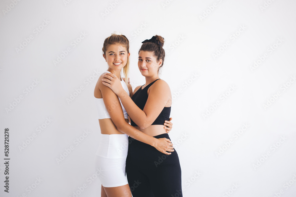 Half length portrait of cheerful fit girls in tracksuits smiling at camera during sportive break in aerobic class, charming Caucaisan female yogi feeling happiness while posing in studio gym Half length portrait of cheerful fit girls in tracksuits smiling at camera during sportive break in aerobic class, charming Caucaisan female yogi feeling happiness while posing in studio gym