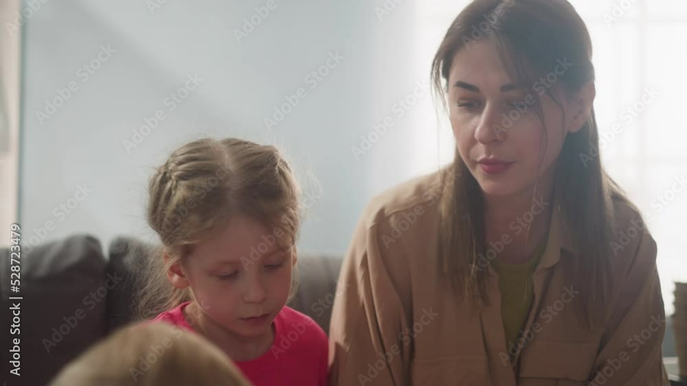 Concentrated mother and daughter look at boy sitting together in living room slow motion. Family education for little children. Woman with children Concentrated mother and daughter look at boy sitting together in living room slow motion. Family education for little children. Woman with children
