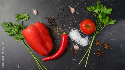 Background for cooking. Fresh red peppers, parsley, cilantro, basil, tomatoes, spices, garlic herbs and vegetables on a black slate table. Top view of food ingredients.