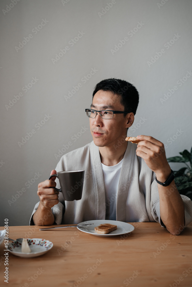 Middle aged asian man with spectacles eating breakfast in kitchen. Middle aged asian man with spectacles eating breakfast in kitchen.
