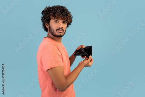Upset indian man showing empty wallet at studio