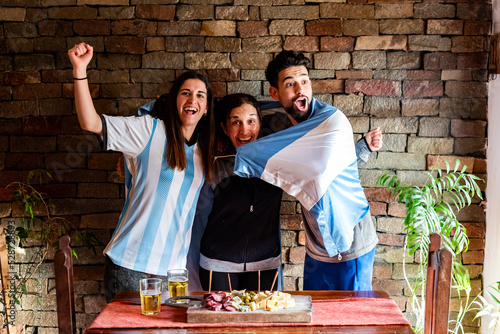 Familia en la previa antes del mundial de futbol, con picadas y cervezas, con los colores celeste y blanco, luz natural, riendo.