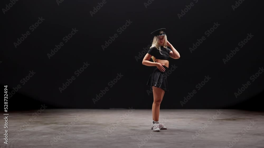 Young Woman in Policemans Hat Dances in Studio Against Black Background Young Woman in Policemans Hat Dances in Studio Against Black Background