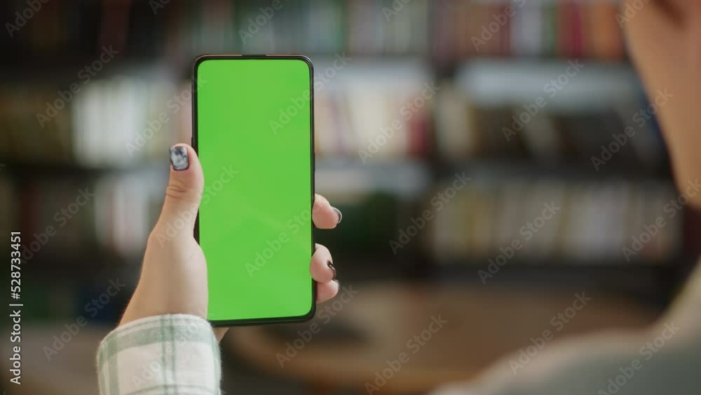Back View of Young Man at Home Office Sitting on Library Collage With Green Mock-up Screen Smartphone. Male is Watcing Content Without Touching Gadget Screen. Modent Technology Back View of Young Man at Home Office Sitting on Library Collage With Green Mock-up Screen Smartphone. Male is Watcing Content Without Touching Gadget Screen. Modent Technology