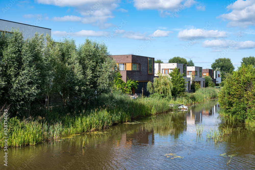 Groningen, The Netherlands, Contemporary country style houses at the waterfront surrounded by nature over blue sky in the suburbs Groningen, The Netherlands, Contemporary country style houses at the waterfront surrounded by nature over blue sky in the suburbs