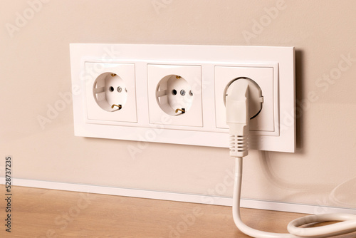 Group of white european electrical outlets with plug inserted into it on modern beige wall. Selective focus © MariiaDemchenko