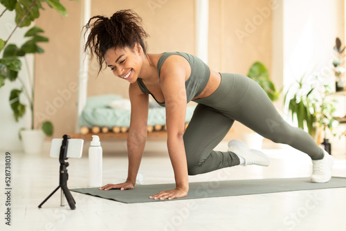 Online workout. Fit african american female doing mountain climbers exercise on yoga mat, looking at smartphone