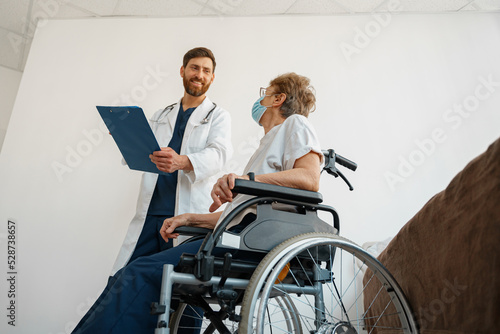 Doctor in uniform explaining to sick patient in wheelchair details of treatment. High quality photo