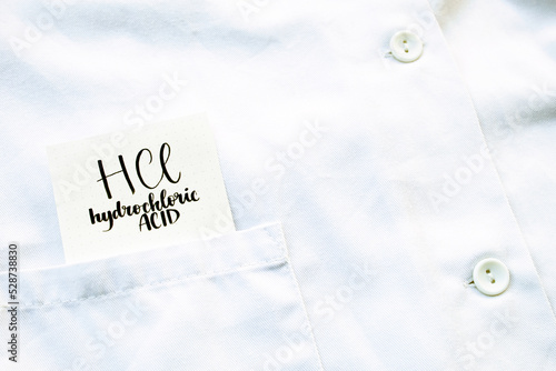 A piece of paper with HCl hydrochloric acid written on it appears from a poket of a laboratory coat. photo
