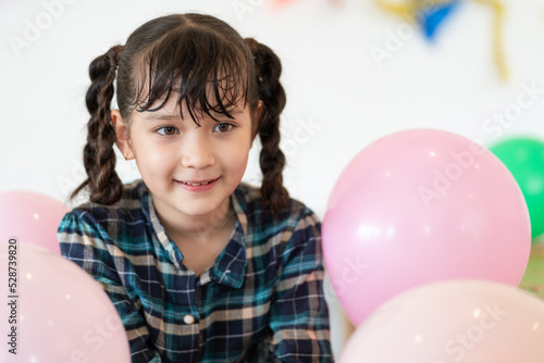 Happy cute little girl sitting with pink balloons at an elementary school party
