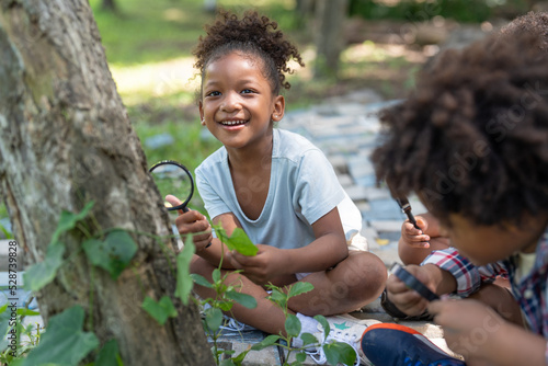 African American little girls with friends exploring and looking bugs on the tree with the magnifying glass between learning beyond the classroom. Education outdoor concept.