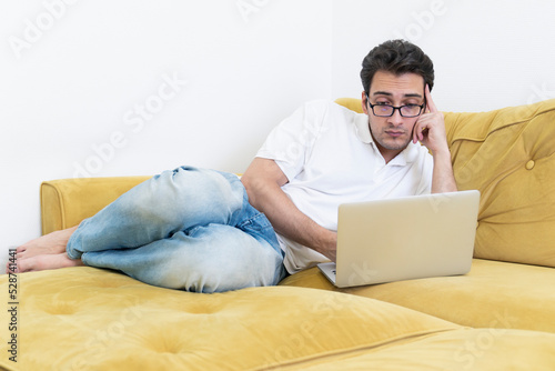 Upset and tired student lying on the couch and studying online at home. Distance learning concept