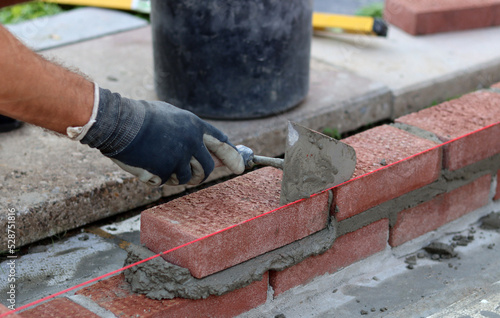 Man works with brick trowel. Masonry work in progress. Wall made of red bricks texture. 