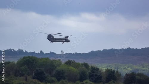 RAF Chinook tandem-rotor CH-47 helicopter flying fast and low in a cloudy blue grey sky on a military battle exercise, Wilts UK