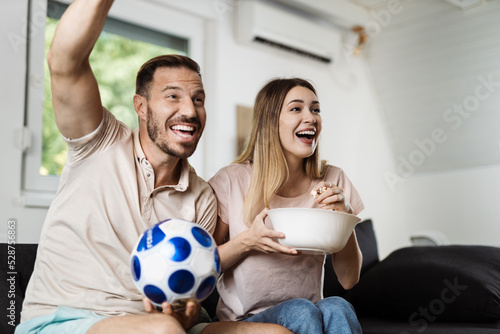Cheerful couple celebrating the victory of their soccer team at home photo