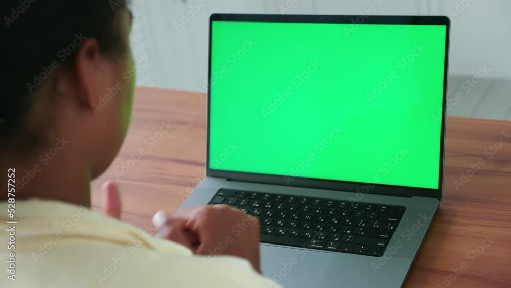 Focus on the green chromakey screen of the laptop monitor and the hands of a copywriter woman sitting with her back to the camera and typing text on keyboard. Copy space for advertising text or video Focus on the green chromakey screen of the laptop monitor and the hands of a copywriter woman sitting with her back to the camera and typing text on keyboard. Copy space for advertising text or video