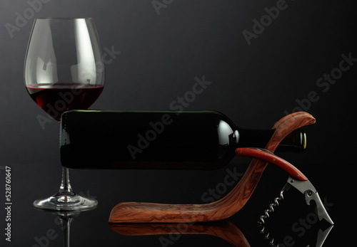 Bottle of red wine in a wooden bottle holder on a black reflective background.