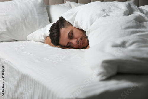 Handsome man sleeping under soft blanket in bed at home