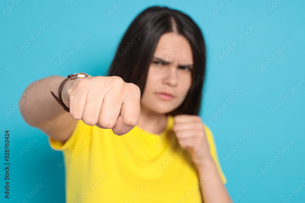 Young woman ready to fight against light blue background, focus on hand. Space for text Young woman ready to fight against light blue background, focus on hand. Space for text