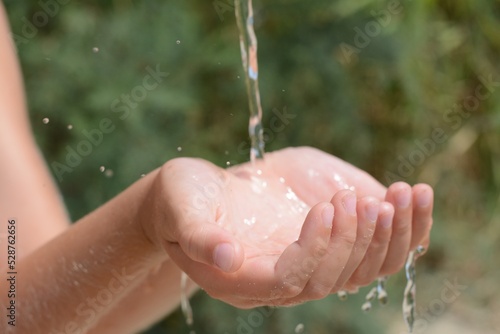 Pouring water into kid`s hands outdoors, closeup