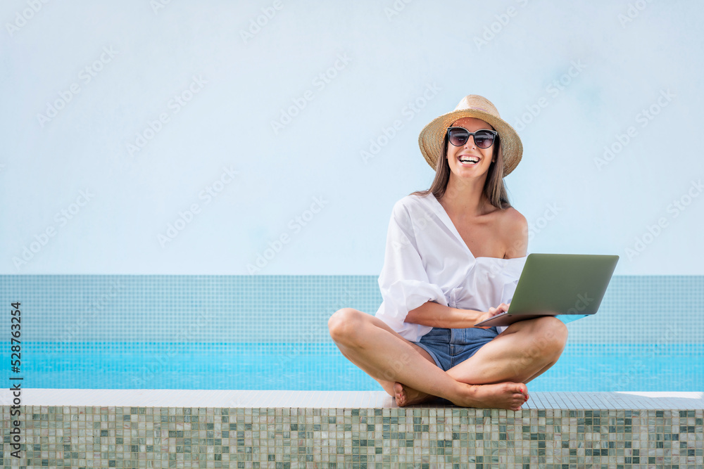 Happy woman using her laptop while sitting at poolside