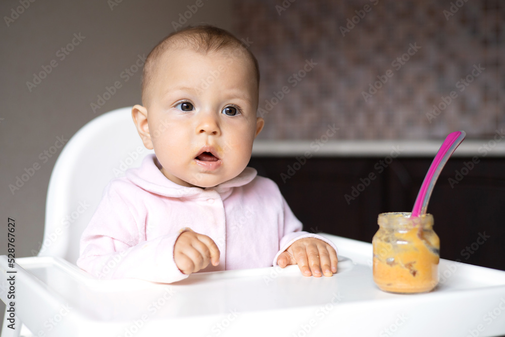Baby food. A baby in a high chair eats vegetable puree from a spoon. Mom feeds the baby from a jar. Kitchen. Lifestyle. Baby food. A baby in a high chair eats vegetable puree from a spoon. Mom feeds the baby from a jar. Kitchen. Lifestyle.