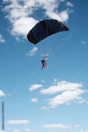Parachute tandem while flying with an open parachute. Blue sky with clouds.