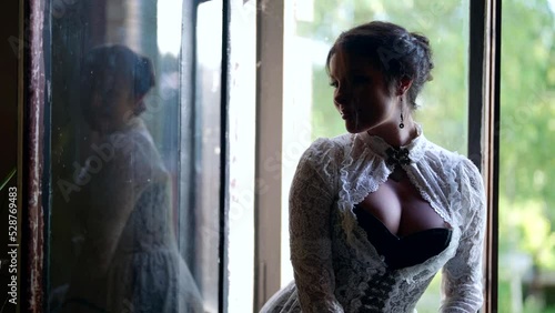 seductive lady with big breasts in vintage dress is resting in village house, sitting on window photo