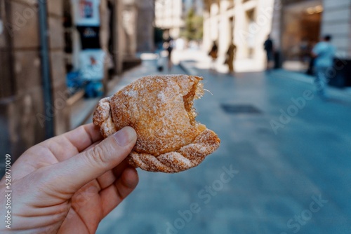Hand of a man in the street holding a pastissets, casquetes, dough pasties with a semicircular shape. The original Aragonese recipe is filled with pumpkin jam, although angel hair filling is common. photo