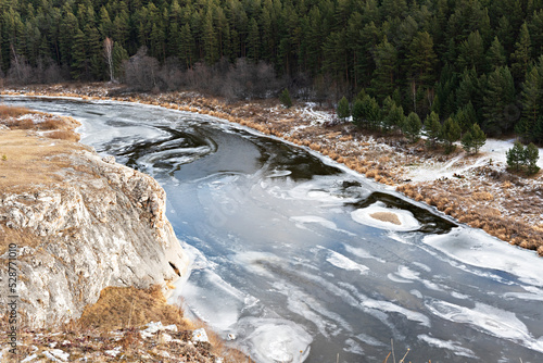 Fototapeta Naklejka Na Ścianę i Meble -  View of river covered with first ice and snow cliffs with dry beige grass and forest in autumn or early winter Landscape earth tones