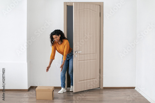 African Lady Receiving Box Standing Near Opened Door At Home
