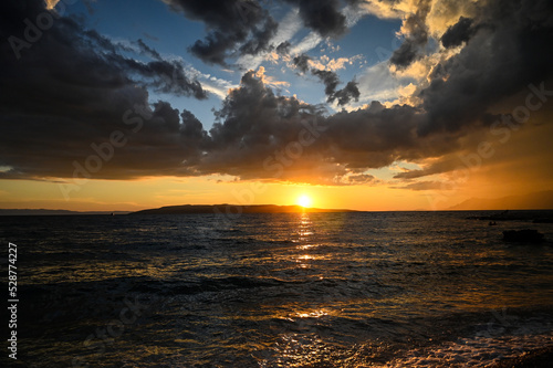 Tropical sunset with dramatic sky with clouds. Sun going down in orange sky over horizon. Silhouette of a island. Soft waves on the water.