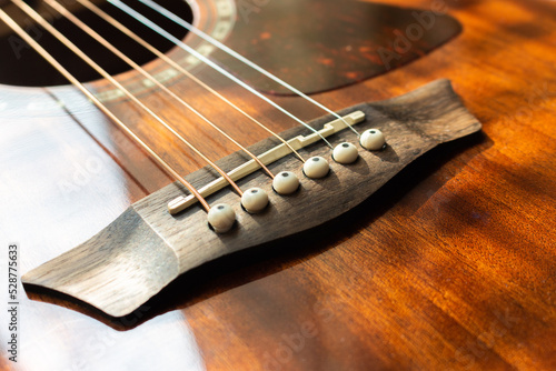 Acoustic guitar bridge with one pins and strings close up with selective shallow focus and blur.