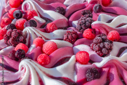 Close up of with pink and white ice cream with forest frozen berries:  black and red currant, blackberry, blueberry, topping sauce. Summer food dessert top. Top view selective shallow focus
