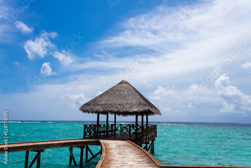 A salt-covered canopy on the edge of a pier on a resort island in the Maldives under a bright blue sky with white clouds and clear turquoise and azure ocean water