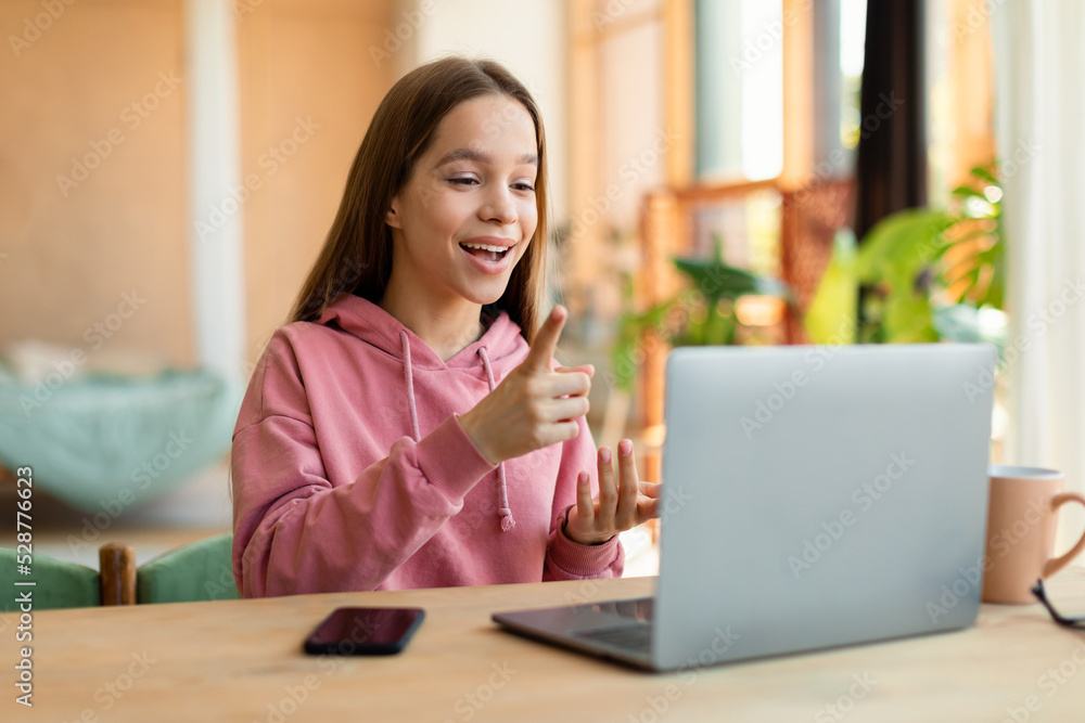 Smart girl teenager having video conference with teacher from home, using laptop and talking at webcamera