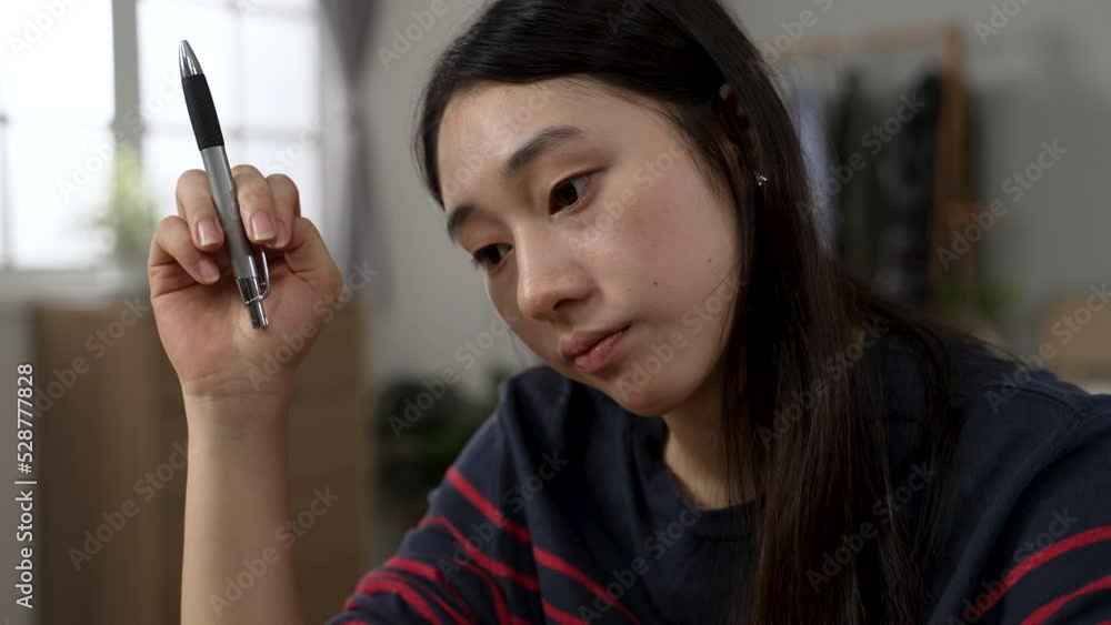 closeup view of a bored Asian college girl learning from home is spinning her pen and staring at empty area while taking online course in the bedroom. closeup view of a bored Asian college girl learning from home is spinning her pen and staring at empty area while taking online course in the bedroom.