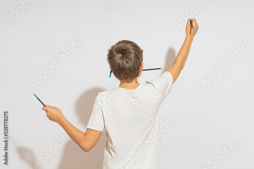 A teenager draws on the wall, standing with his back to the camera. Hard light, white background.