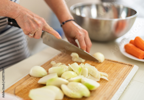 Close-up of a woman cutting onions with a kitchen knife in a bright kitchen.