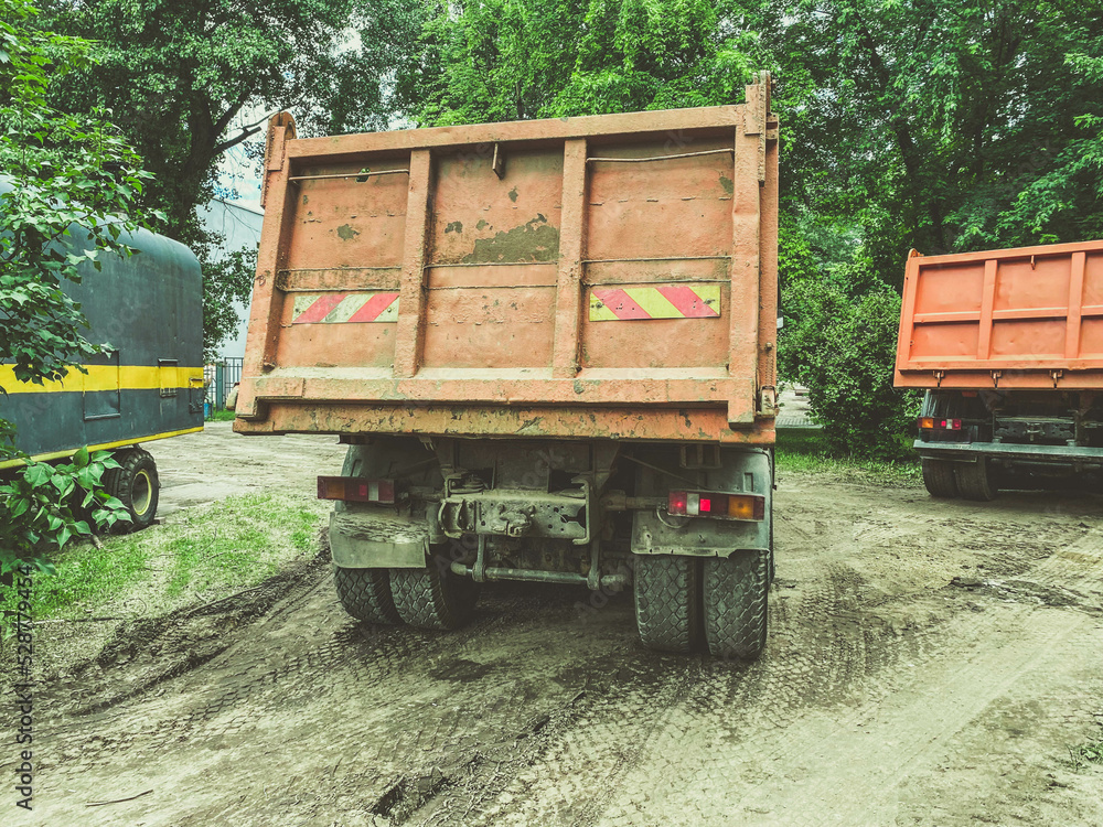 a huge truck with a body for transporting heavy things. heavy-duty vehicle sticker on the back of the body. the car is driving on a dirty, wet road