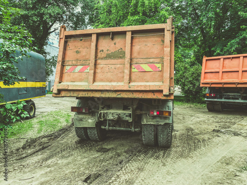 a huge truck with a body for transporting heavy things. heavy-duty vehicle sticker on the back of the body. the car is driving on a dirty, wet road © Aliaksandra