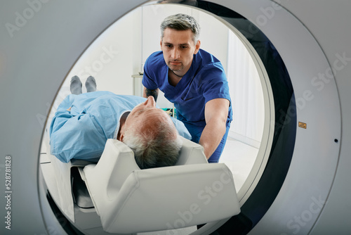 Senior man going into CT scanner. CT scan technologist overlooking patient in Computed Tomography scanner during preparation for procedure photo
