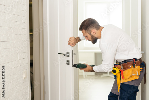 good looking man working as handyman and fixing a door lock in a house entrance photo