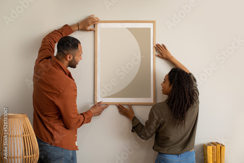 African American Couple Hanging Poster On Wall At Home