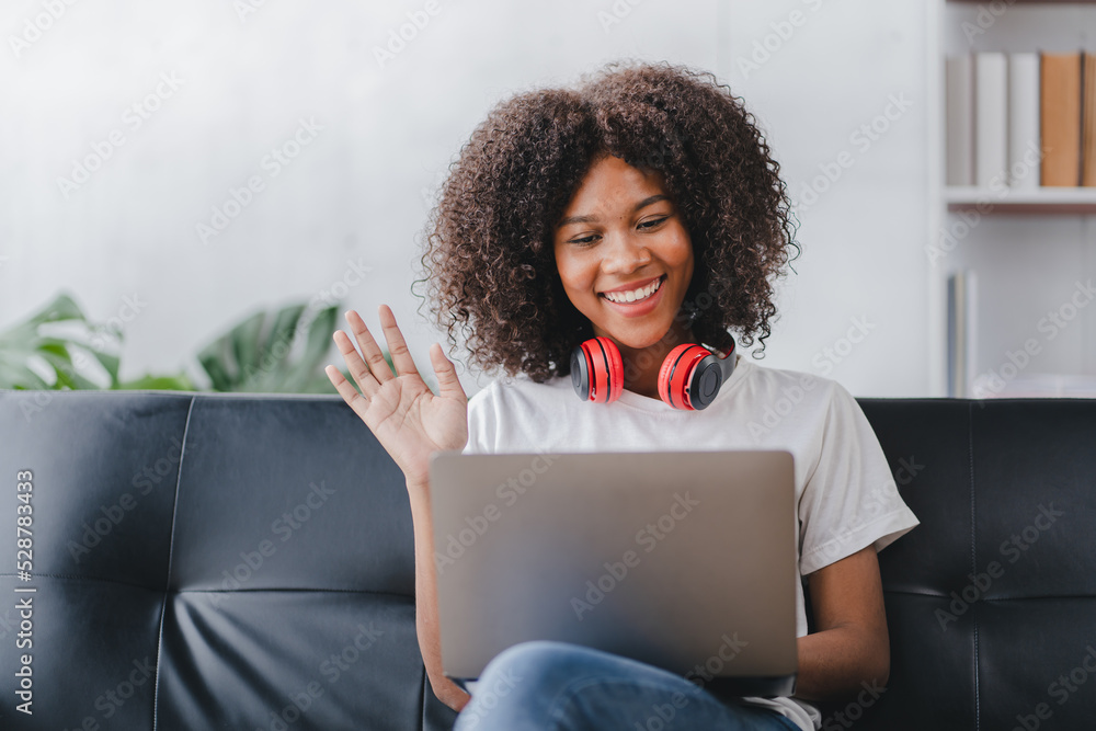 african american woman sitting on sofa at home video call chatting with friends using a laptop and a smartphone or phone african american woman sitting on sofa at home video call chatting with friends using a laptop and a smartphone or phone